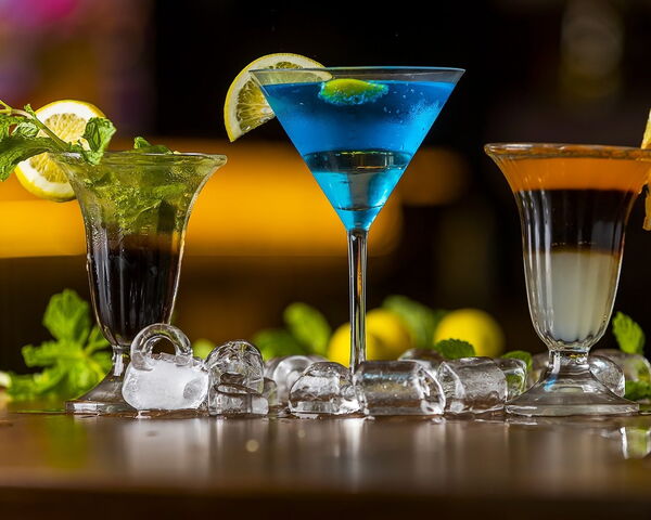 Drei Cocktails mit Zitrone und Minze auf der Bar, in der Mitte ein blauer Cocktail