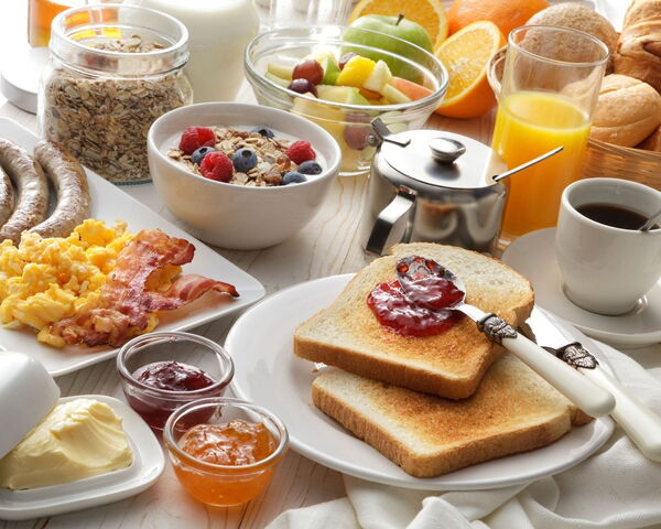 Frühstücksbuffet mit Rührei, Speck, Würstchen, Müsli, Obst, Toast mit Marmelade, Orangensaft und Kaffee