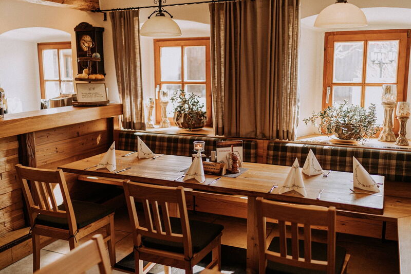 Helle Gaststube mit Holztischen, Fensterbänken und Wanduhr