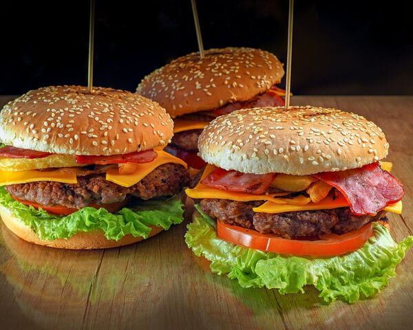 Drei Burger mit Rindfleisch, Speck, Cheddar, Tomate und Salat auf einem Holztisch